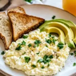 A creamy serving of cottage cheese eggs garnished with fresh parsley on a white plate