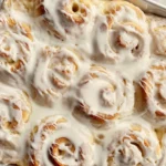 Freshly baked cinnamon rolls with heavy cream poured over them, highlighting the secret to moist and flavorful rolls.