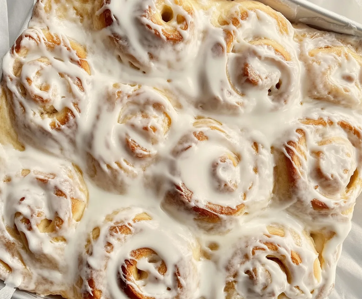 Freshly baked cinnamon rolls with heavy cream poured over them, highlighting the secret to moist and flavorful rolls.
